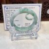 A green jade bracelet is displayed on a clear glass stand.