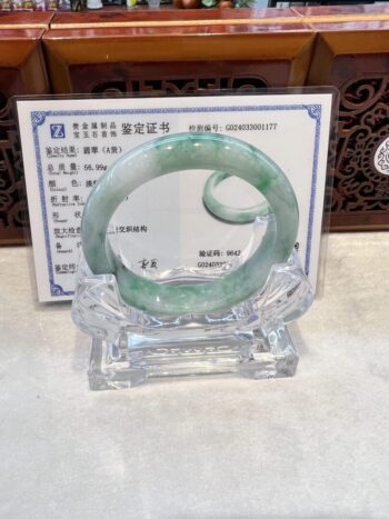 A green jade bracelet is displayed on a clear glass stand.