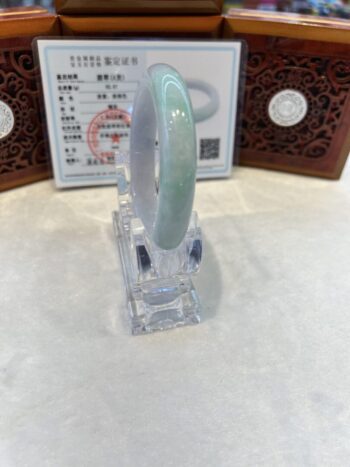 A green jade bracelet is on display in front of an asian screen.