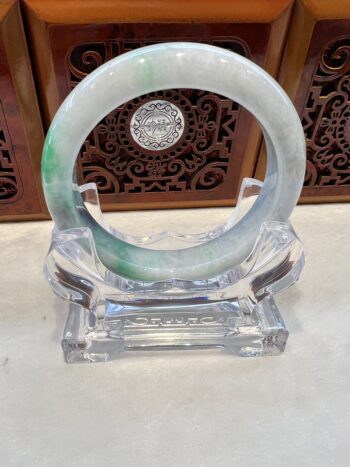 A green and white bangle sitting on top of a clear glass holder.