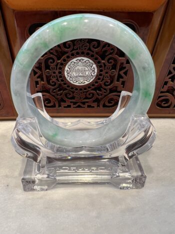 A green and white bracelet sitting on top of a clear glass stand.