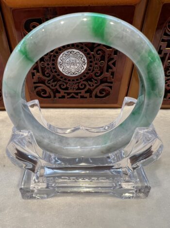 A green and white bracelet sitting on top of a clear glass.