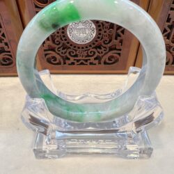 A green and white bracelet sitting on top of a clear glass.