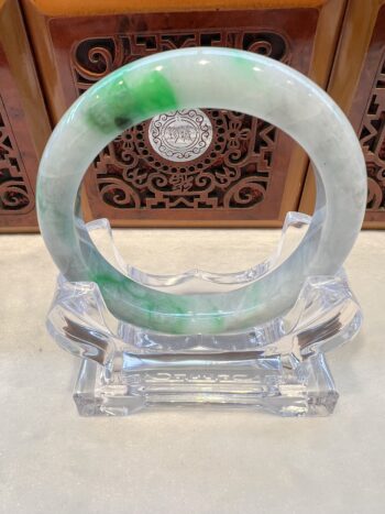 A green and white bracelet sitting on top of a clear glass.