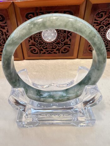 A green jade bangle sitting on top of a clear glass stand.