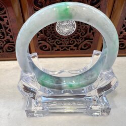 A green and white bracelet sitting on top of a clear stand.