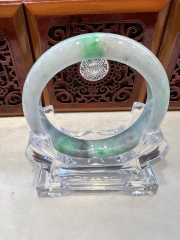 A green and white bracelet sitting on top of a clear stand.