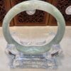 A green jade bangle sitting on top of a clear glass stand.