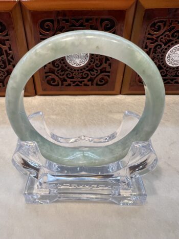 A green jade bangle sitting on top of a clear glass stand.