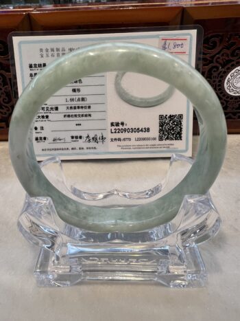 A green jade bracelet sitting on top of a clear glass display.