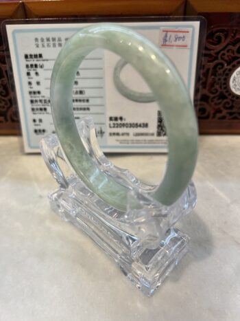 A green jade bangle is sitting in a clear plastic holder.