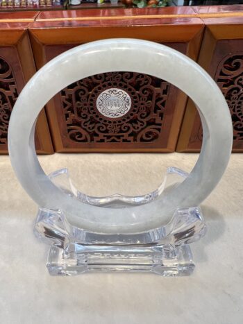 A white jade bangle sitting on top of a clear glass base.