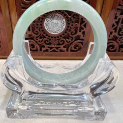 A green jade bangle sitting on top of a glass stand.