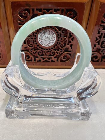 A green jade bangle sitting on top of a glass stand.