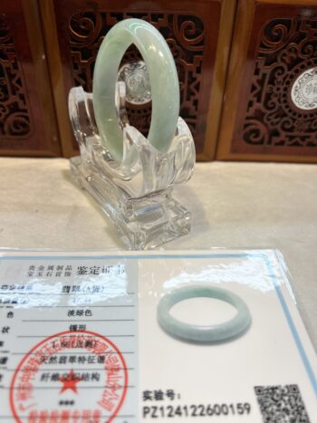 A green jade bracelet sitting on top of a clear glass.