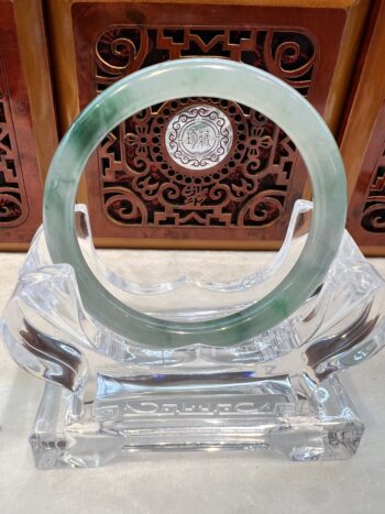 A green and white jade bracelet sitting on top of a clear glass.