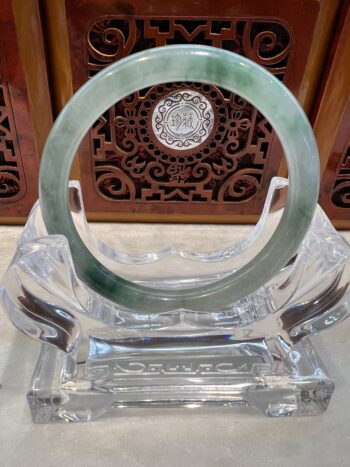 A green and white jade bracelet sitting on top of a glass table.