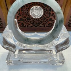 Jade bracelet on ornate wooden stand display.