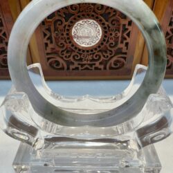Jade bangle displayed on carved wooden stand.