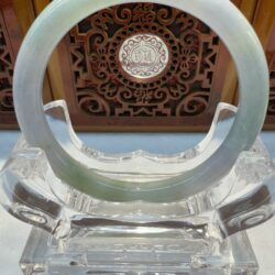 Light green jade bracelet against carved wooden panel