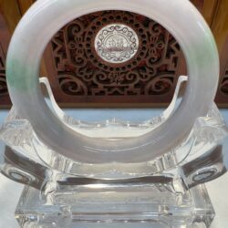 Round pale jade bracelet against wooden carving