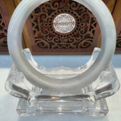 Round jade bangle displayed before carved wood