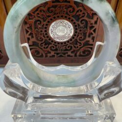 Circular jade ornament on carved wooden stand.
