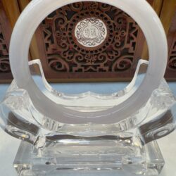 Circular jade sculpture on ornate wooden stand.