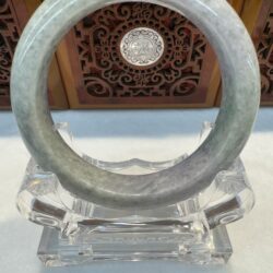 Grey-green jade bangle front view with carved backdrop