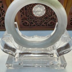 Pale green jade bangle against carved wood panel