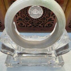 Jade bangle on clear stand, ornate background.