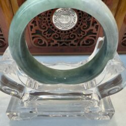 Dark green jade bangle angled on acrylic stand