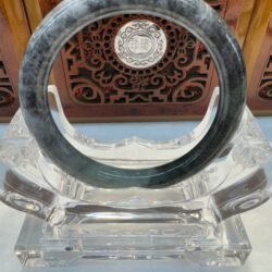 Gray jade bangle on clear display stand.