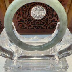 Green jade bangle displayed on glass stand.