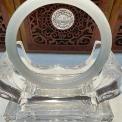 Circular white jade bangle with carved wooden backdrop