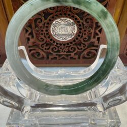 Dark-veined jade bangle displayed on acrylic base