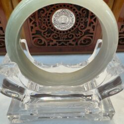 Round jade bracelet displayed against carved panel