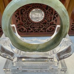 Green jade bracelet on ornate wooden stand.