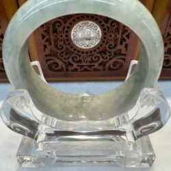 Green jade bangle on decorative wooden stand.