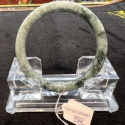 Green jade circular bracelet on a clear acrylic stand in a shop display, with a price tag attached.