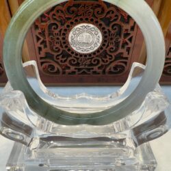 Jade bracelet on ornate stand, decorative background.