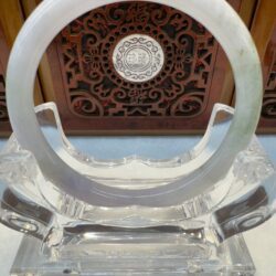 Jade bracelet displayed on carved wooden stand.