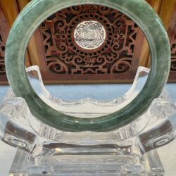 Polished pale green jade bracelet on acrylic stand