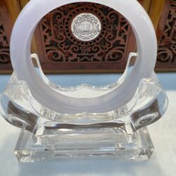 Clear display stand with circular jade ornament.