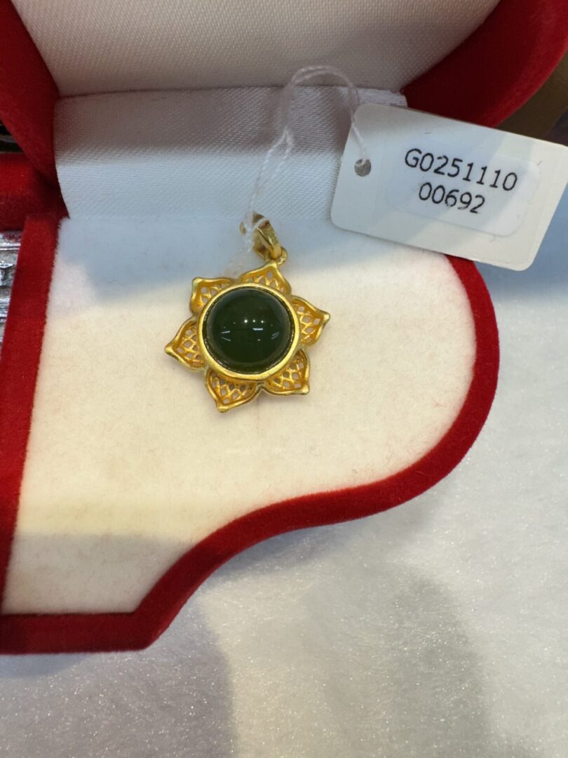 Gold pendant with green gemstone in box.