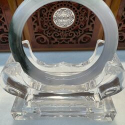 Ornate jade ring on clear display stand.