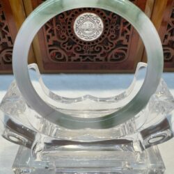 Jade bangle displayed on ornate wooden backdrop.