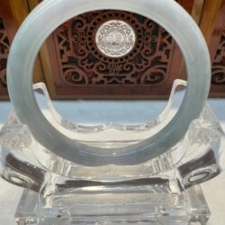 Translucent pale green jade bangle on clear stand