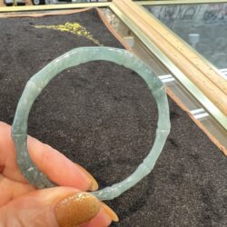 Translucent light-blue jade bracelet shaped like bamboo segments, held by a hand over a shop counter.
